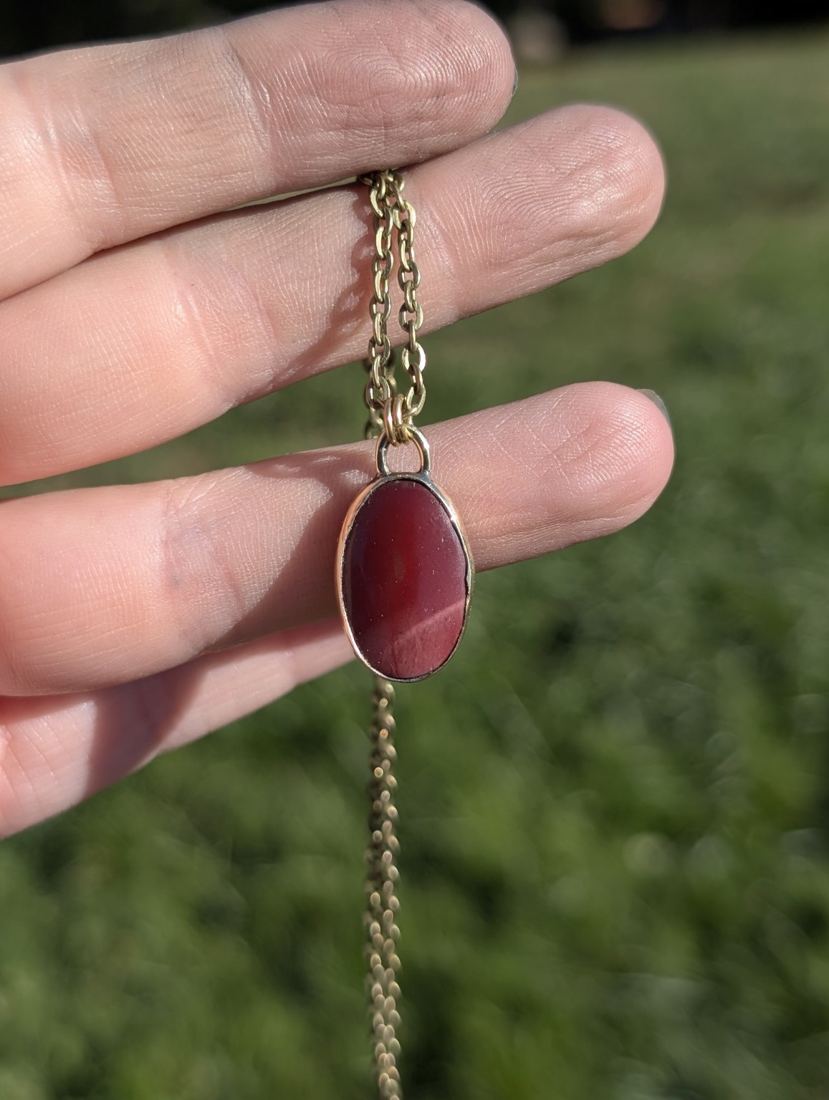 Close-up of a handmade red stone pendant held in Jacquline’s hand.