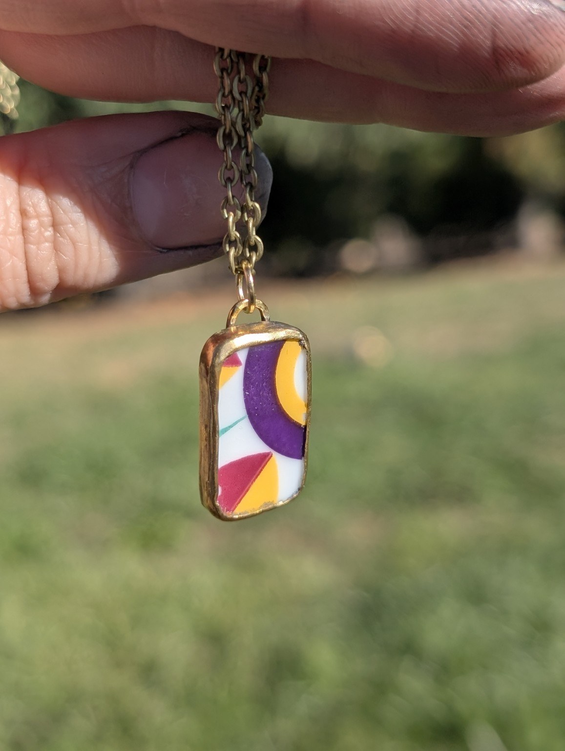Colorful reclaimed china pendant with purple, yellow, and red shapes in a brass setting.